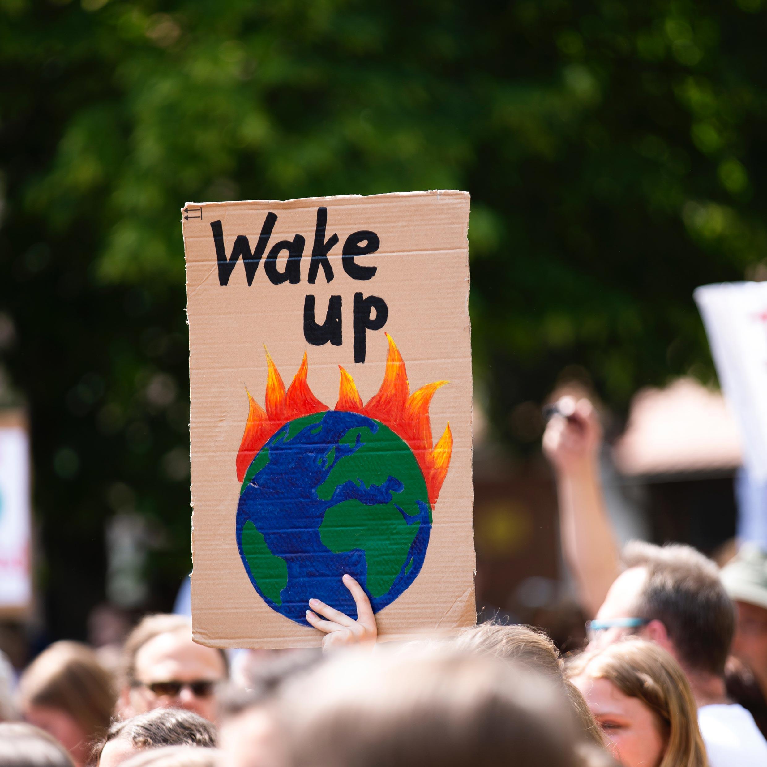 Protester holding sign with earth on fire saying wake up